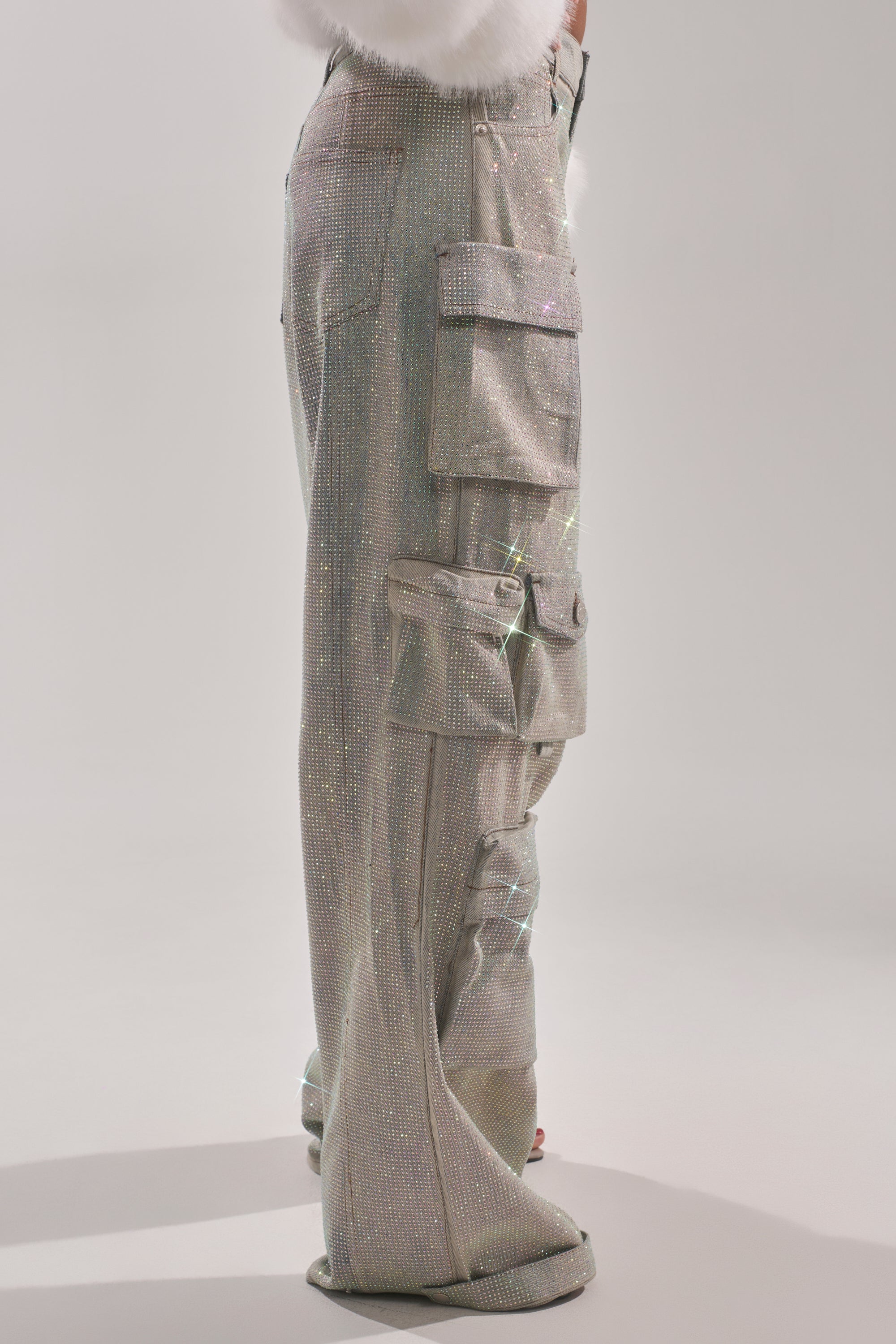 Only the lower half of a person is visible as they stand against a plain light background, dressed in BLING BLING CARGO DENIM featuring sparkling silver fabric, multiple oversized pockets, and a wide-leg silhouette. 2