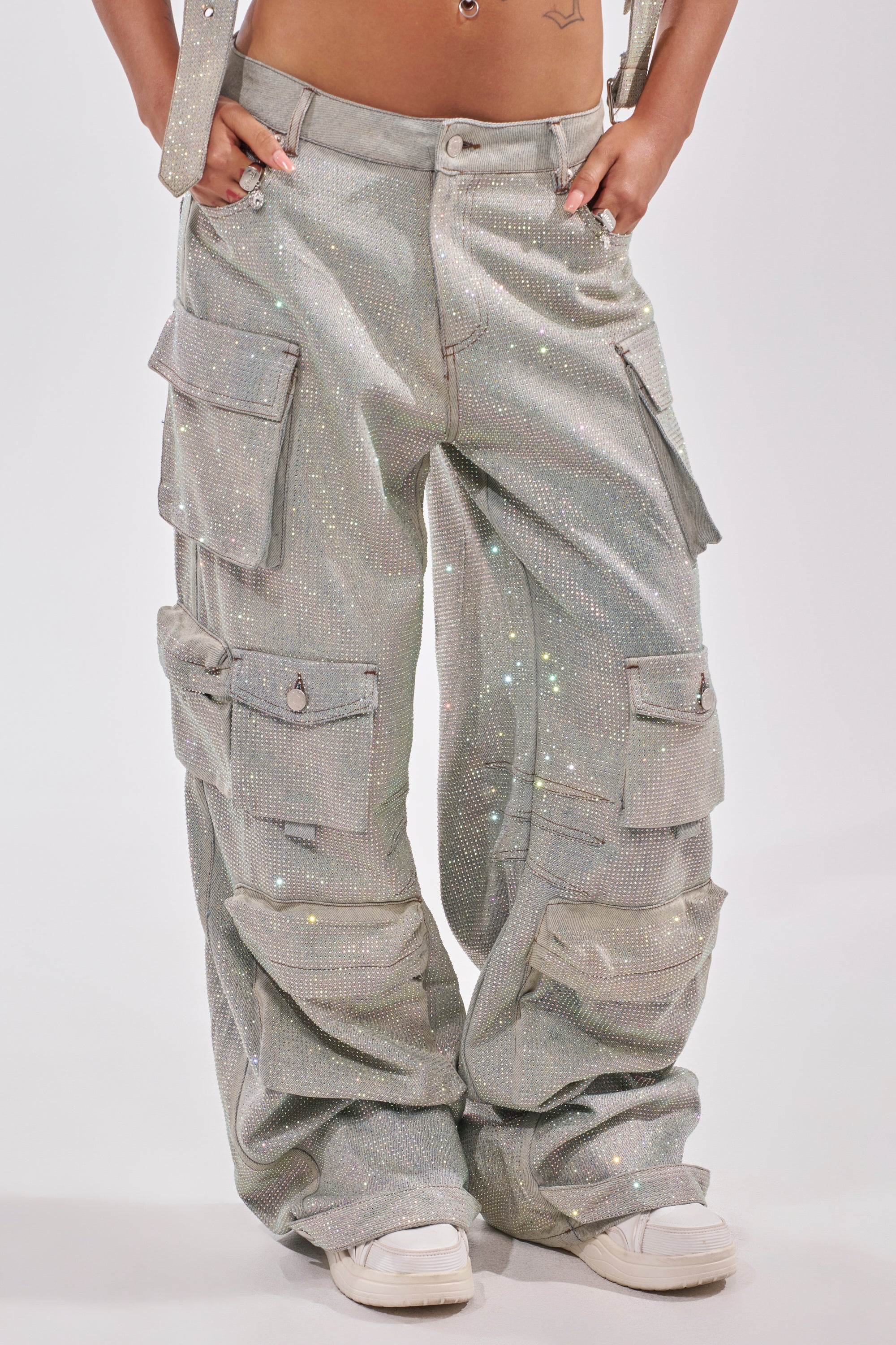 A person wears BLING BLING CARGO DENIM—loose, sparkly silver wide-leg pants with multiple pockets—paired with white sneakers, posing against a plain light background. Only the lower torso and legs are shown. 2
