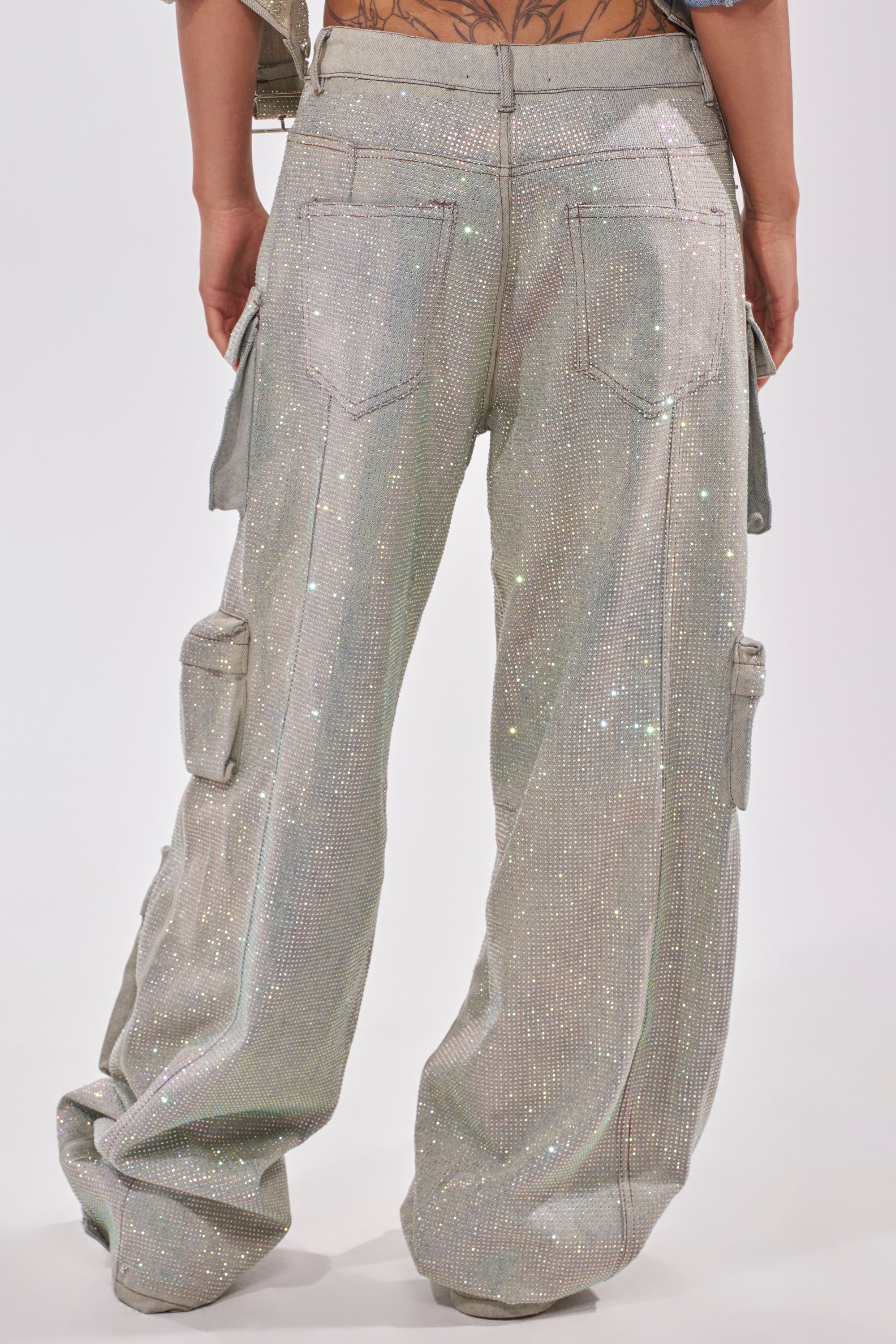 A person shown from behind wearing BLING BLING CARGO DENIM—loose-fitting, high-rise pants in sparkling silver with back and side pockets, featuring a shimmery texture that adds a bold twist to classic cargo style. 4