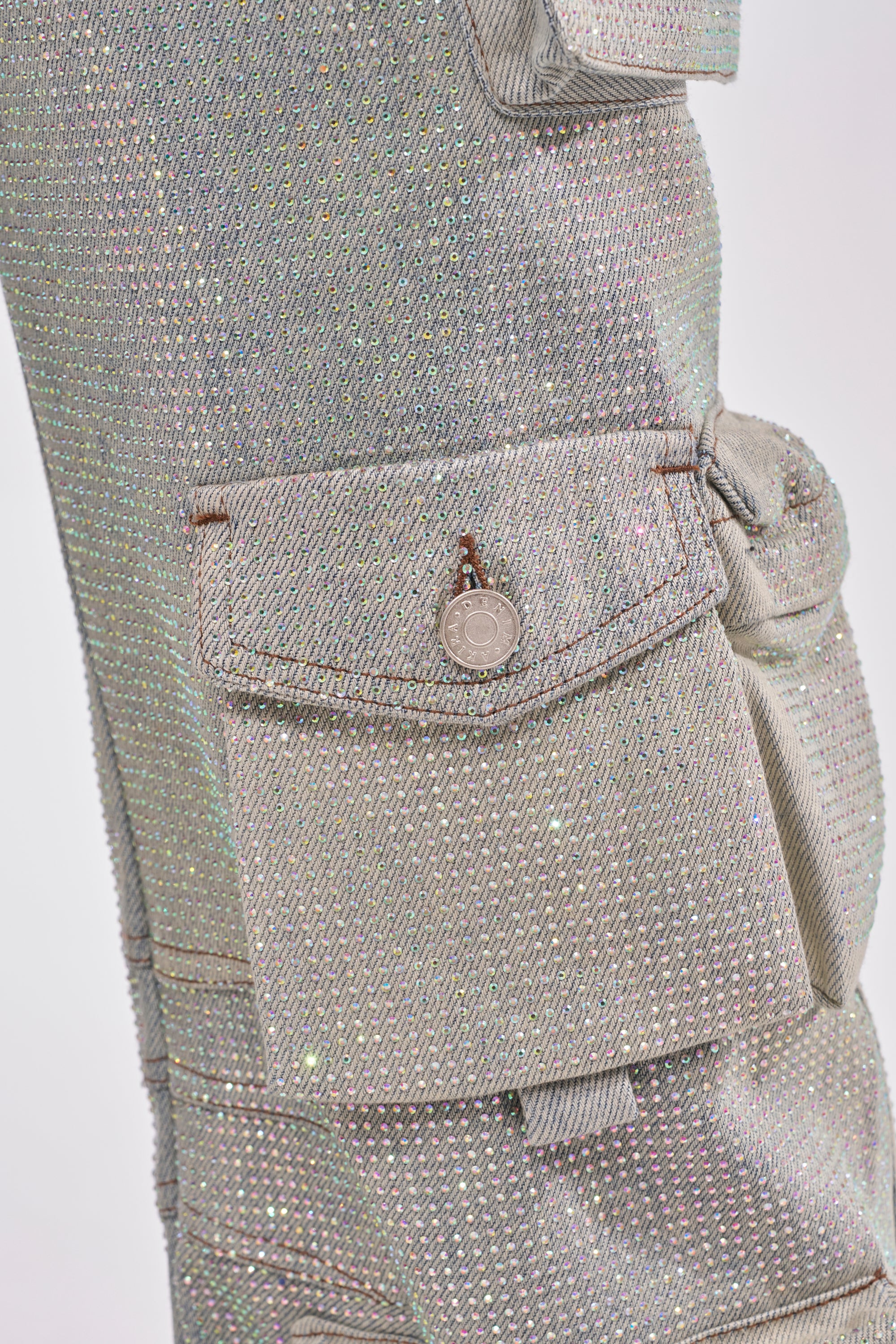 Close-up of BLING BLING CARGO DENIM with iridescent, glittery finish, multiple cargo pockets with visible stitching, and a metallic button detail. 7