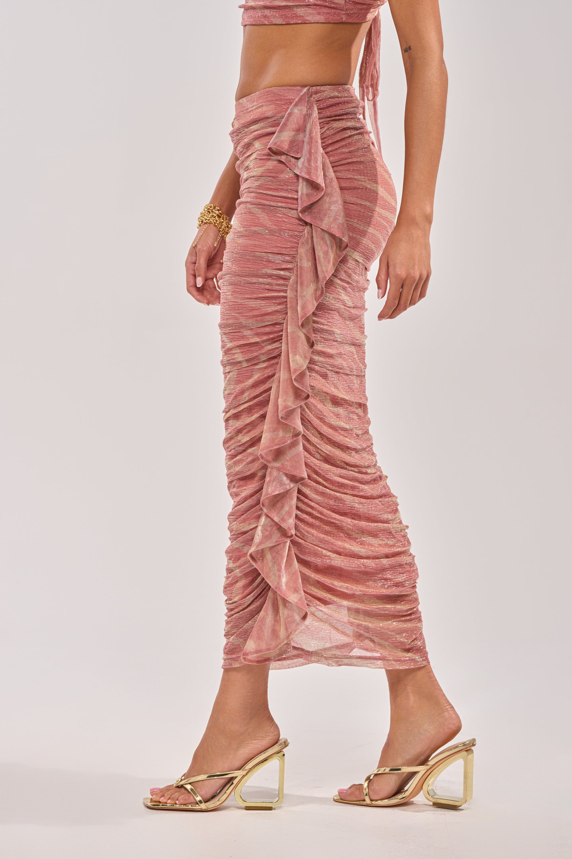 A woman wearing the PLAY WITH ME MAXI SKIRT with a matching crop top and gold high-heeled sandals stands against a light background—an effortlessly chic vacation look. 3