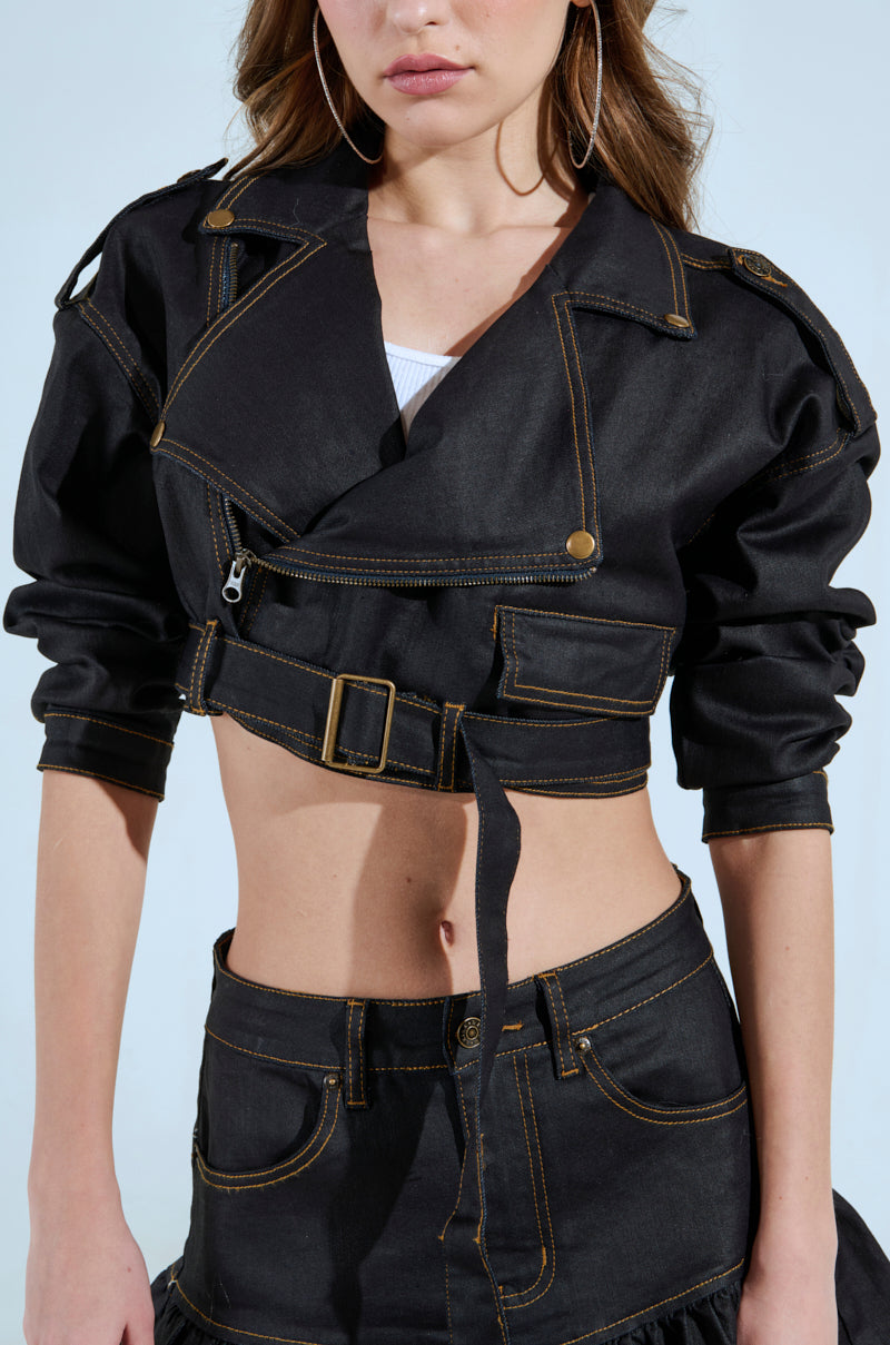 The BETTER DAYS AHEAD COATED DENIM MOTO collection includes a chic cropped black denim moto jacket with gold stitching and belt, paired with a matching high-waisted pencil skirt. Detailed pockets and large hoop earrings enhance her look, while her hair flows in loose waves.
