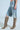Someone wearing the ALL IVE GOT DENIM BERMUDA SHORT with a detachable chain attachment on the pocket and knee-high brown snakeskin boots with pointed toes and stiletto heels stands against a plain background.