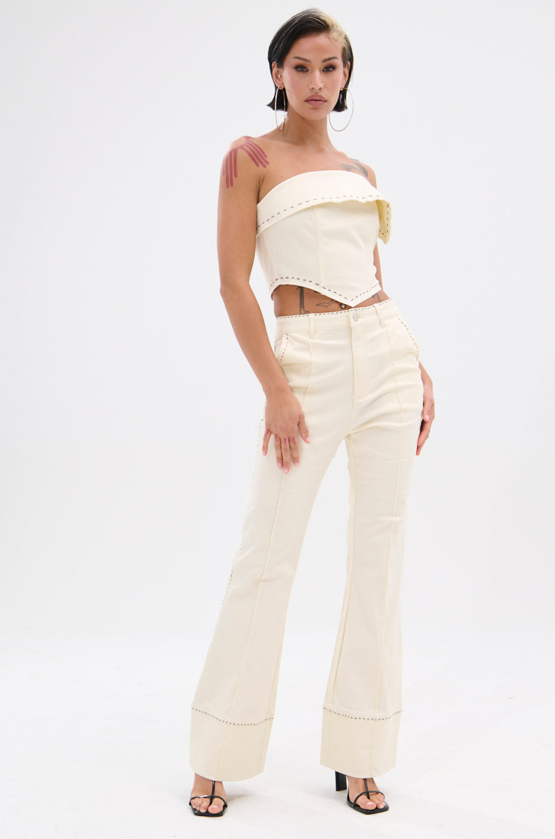 A woman stands against a plain white background, wearing the BREAK MY LOVE LINEN TUBE TOP with metal rivet details and matching high-waisted flared pants. She has short dark hair, statement earrings, and strappy black heels. 6