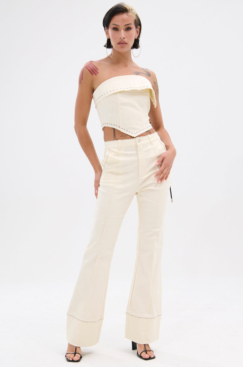 A woman stands confidently against a white background, wearing the BREAK MY LOVE LINEN TUBE TOP in cream with matching high-waisted pants featuring visible seams and stud accents. She has tattoos and pairs the outfit with open-toe heels. 8