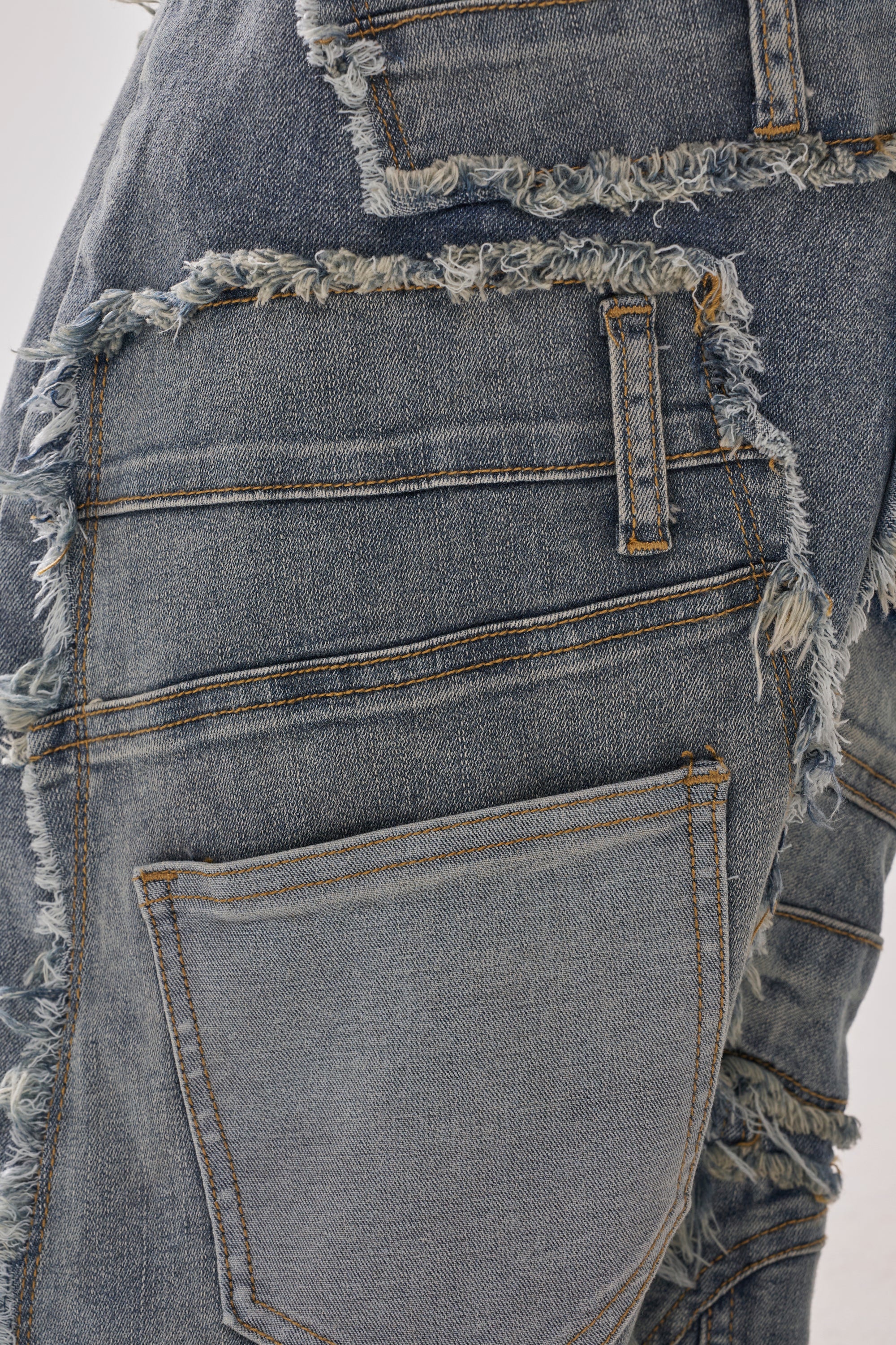 Close-up of ALL OVER ME DENIM PATCHWORK JEANS with large frayed seams, oversized unevenly stitched pockets, distressed edges, and a rugged patchwork design for a worn-in look.