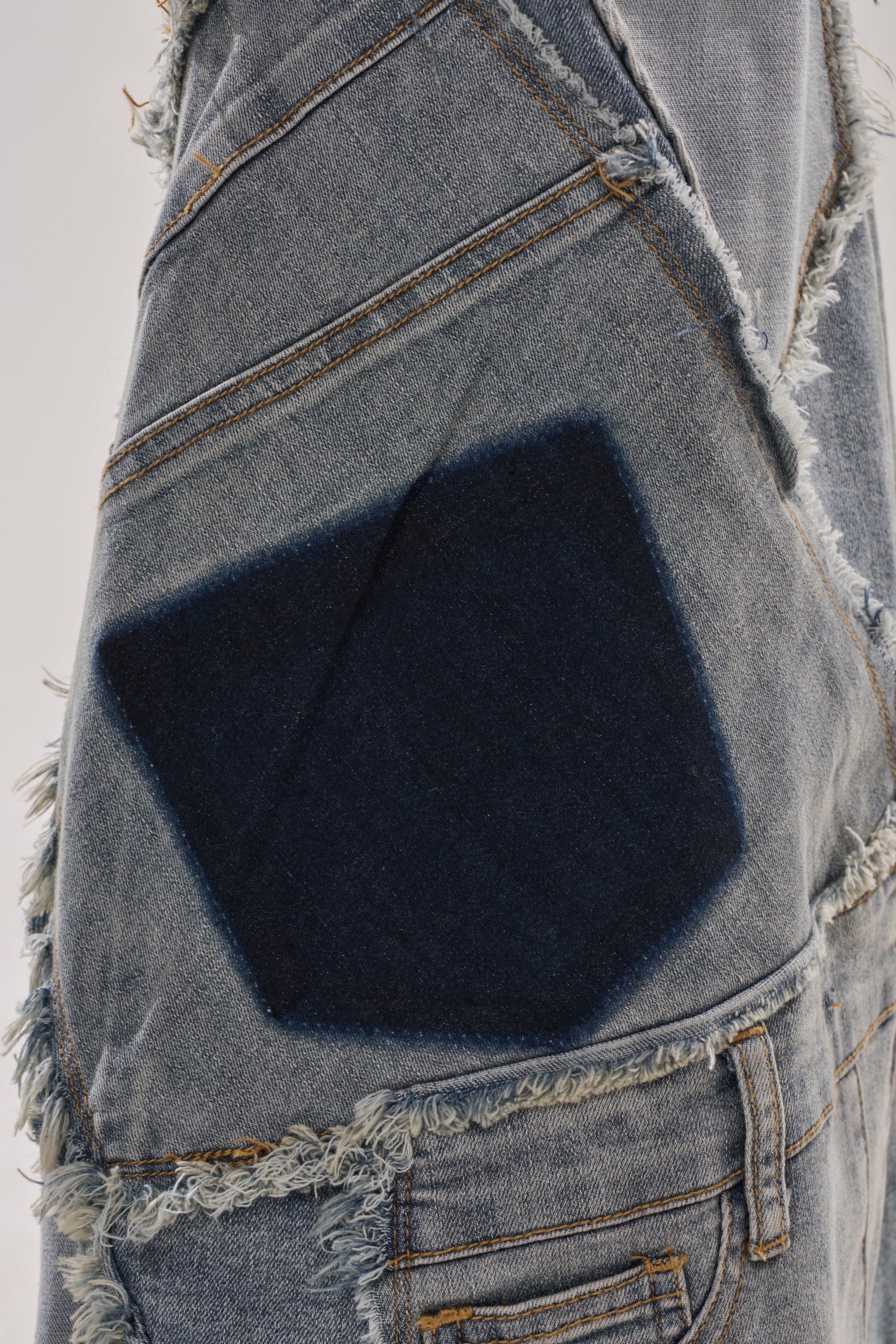 Close-up of ALL OVER ME DENIM PATCHWORK JEANS, featuring frayed blue denim, a large dark blue patch, and visible stitching details on distressed light blue fabric.