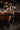 A woman stands in front of a bar, wearing the DONT THINK ABOUT IT COW PRINT MINI SKIRT IN BROWN with a sleeveless vest and tall black fringe boots. The bar features wooden chairs, glasses, beer taps, and a 
