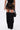 A person wears the DONT THINK ABOUT IT COW PRINT MINI SKIRT IN BROWN, paired with a black handbag and tall, fluffy black faux fur boots above the knees. Their upper body is partially out of frame.