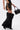 A person wears the DONT THINK ABOUT IT COW PRINT MINI SKIRT IN BROWN, styled with black furry leg warmers over heeled boots, a black top, and holds a black handbag against a white background.