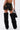 A person models the DONT THINK ABOUT IT COW PRINT MINI SKIRT IN BROWN, paired with tall black faux fur boots and a black handbag, standing against a plain white background.