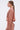 A woman with straight brown hair in a low ponytail wears AKIRA Label’s NOT ALONE BUTTON DOWN TOP in textured dusty pink with matching high-waisted pants, styled with large geometric earrings as she stands in profile.
