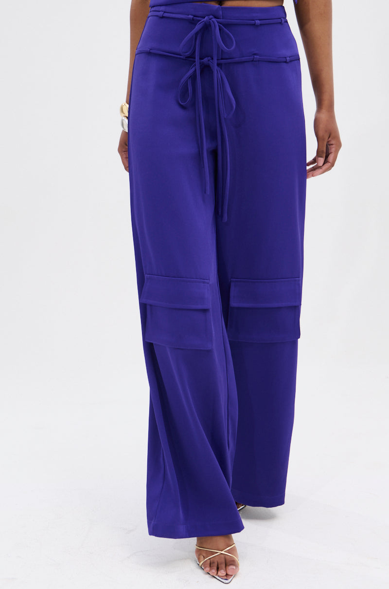 A person wears the NEEDED THIS CARGO TROUSER—high-rise, wide-leg royal blue pants with front pockets and a tie belt—paired with strappy heeled sandals against a plain white background.