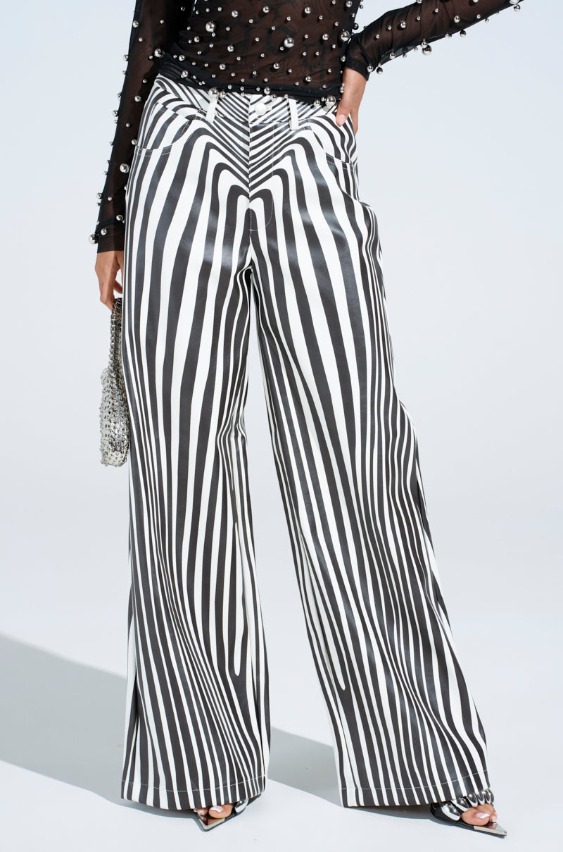 Close-up of a person wearing the PARADOX STRIPE PANT, black and white vertically striped wide-leg pants, and a black sheer top with pearl embellishments. They're holding a sparkling silver handbag, with open-toe black strappy shoes.