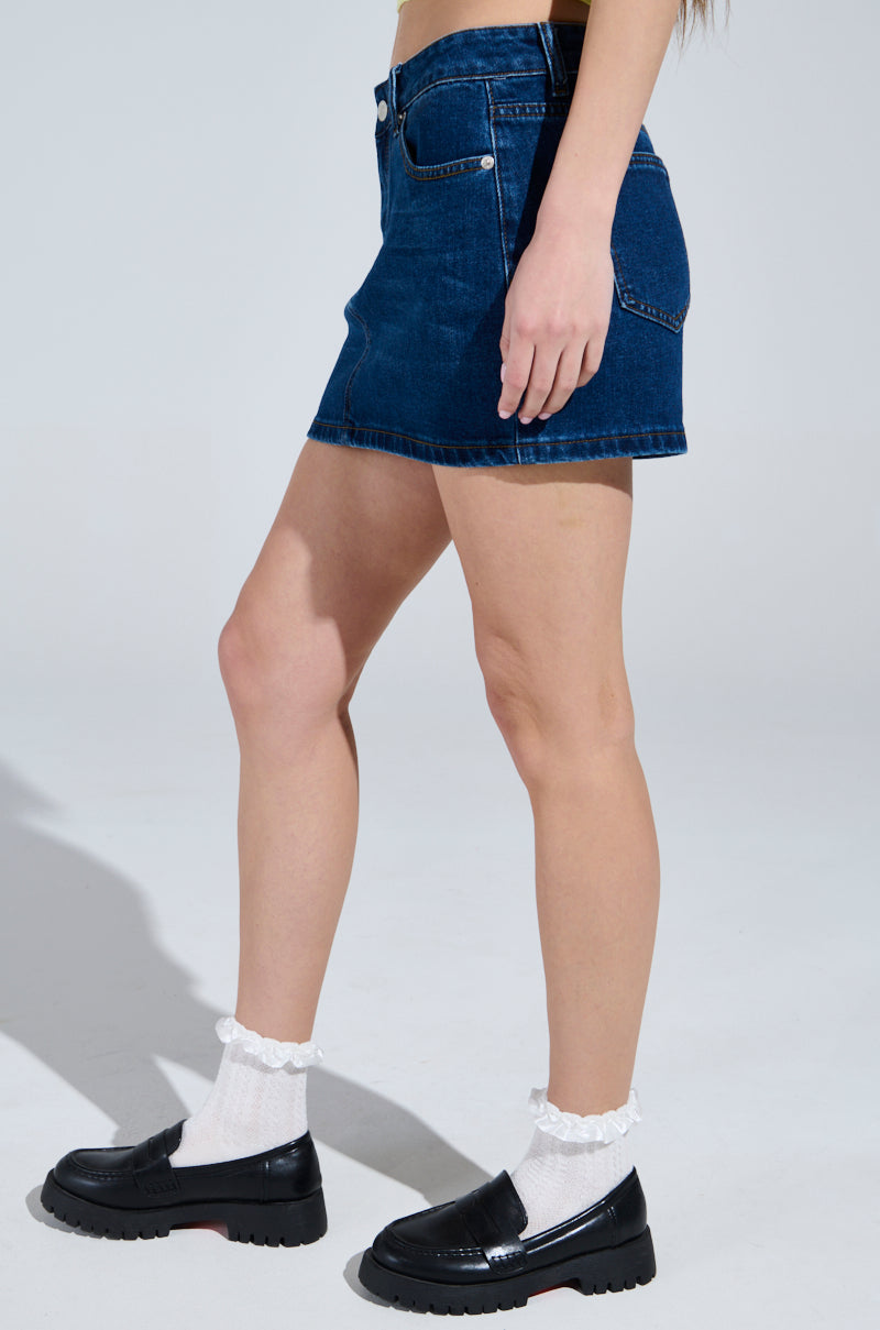 A person wearing the JOLENE DENIM MINI SKIRT with a five-pocket design is styled with white ruffled socks and black loafers, captured from the waist down on a neutral background.