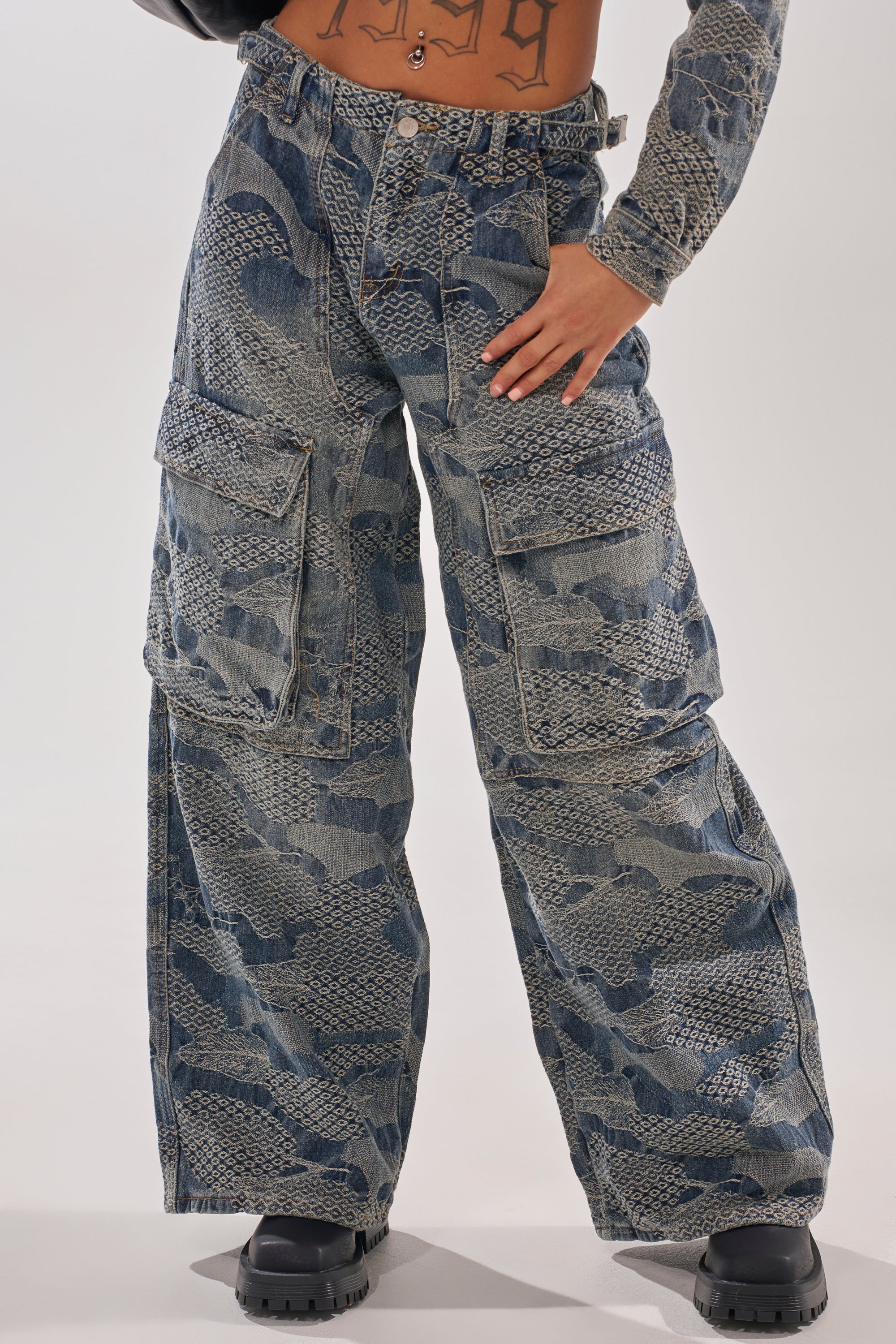 Wearing the I THINK YOU WANNA KNOW DENIM CARGO PANT in blue snakeskin print with multiple large pockets, paired with black chunky boots and a printed crop top, hand on hip for a bold cargo look. 5