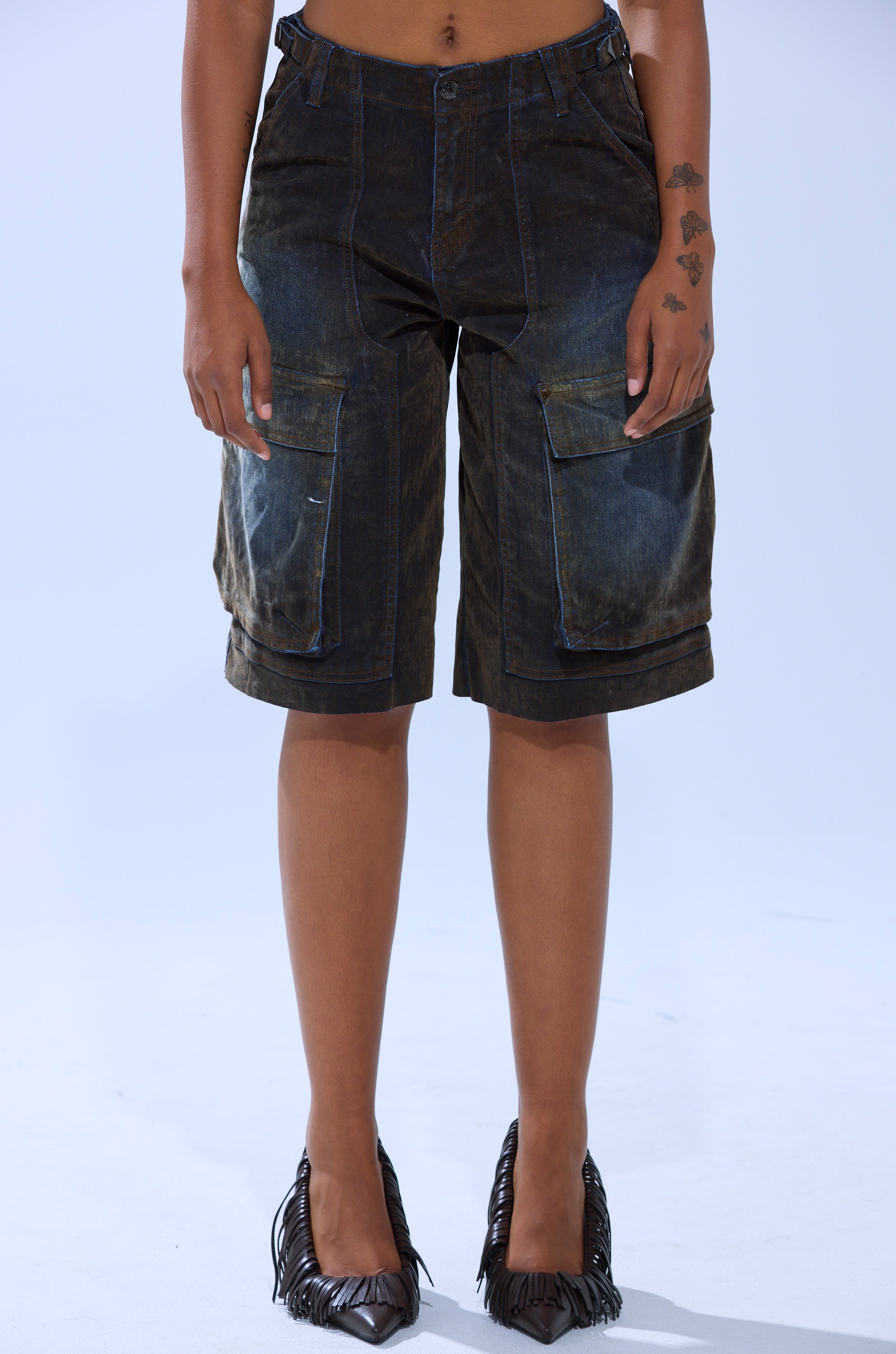 Wearing the BELLA VELVET DENIM JORT in dark denim with black fringe high heels, a person stands against a plain light background. The upper body and hands are partially out of frame.