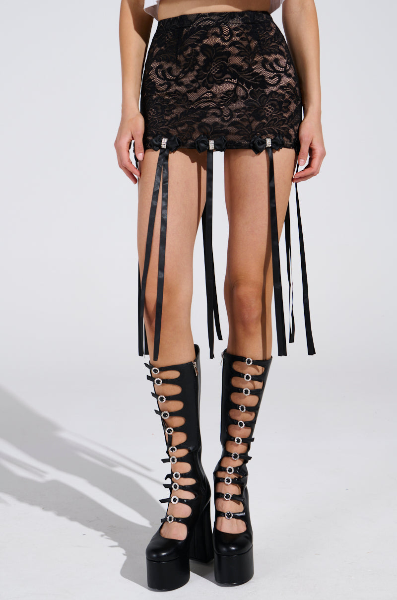 The image features a person in the GIRLY POP LACE MINI SKIRT, a black floral lace mini with garter straps, against a light background. They also wear tall black platform boots adorned with multiple straps and silver buckles, focusing on their lower half.
