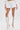 A person wearing the PLAY WITH ME SHORT white high-rise shorts, a white long-sleeve crop top, knee-high white lace-up heeled boots, and holding a small white handbag against a plain white background.