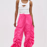 A woman faces forward in white sneakers and the GIRL ON FIRE RUCHED JOGGER, styled with a white ripped tank top. Her long straight hair and neutral expression complete an effortlessly cool streetwear look against a plain light background.