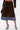 Someone models the FALL VIBES VELVET BERMUDA SHORT, paired with a black handbag and black high heels featuring round silver embellishments, against a plain white background.