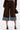 A person stands facing away, wearing the FALL VIBES VELVET BERMUDA SHORT with large back pockets and a denim hem, styled with a brown belt, shirt, silver high-heeled sandals, and a small black handbag—perfect for fall fashion.