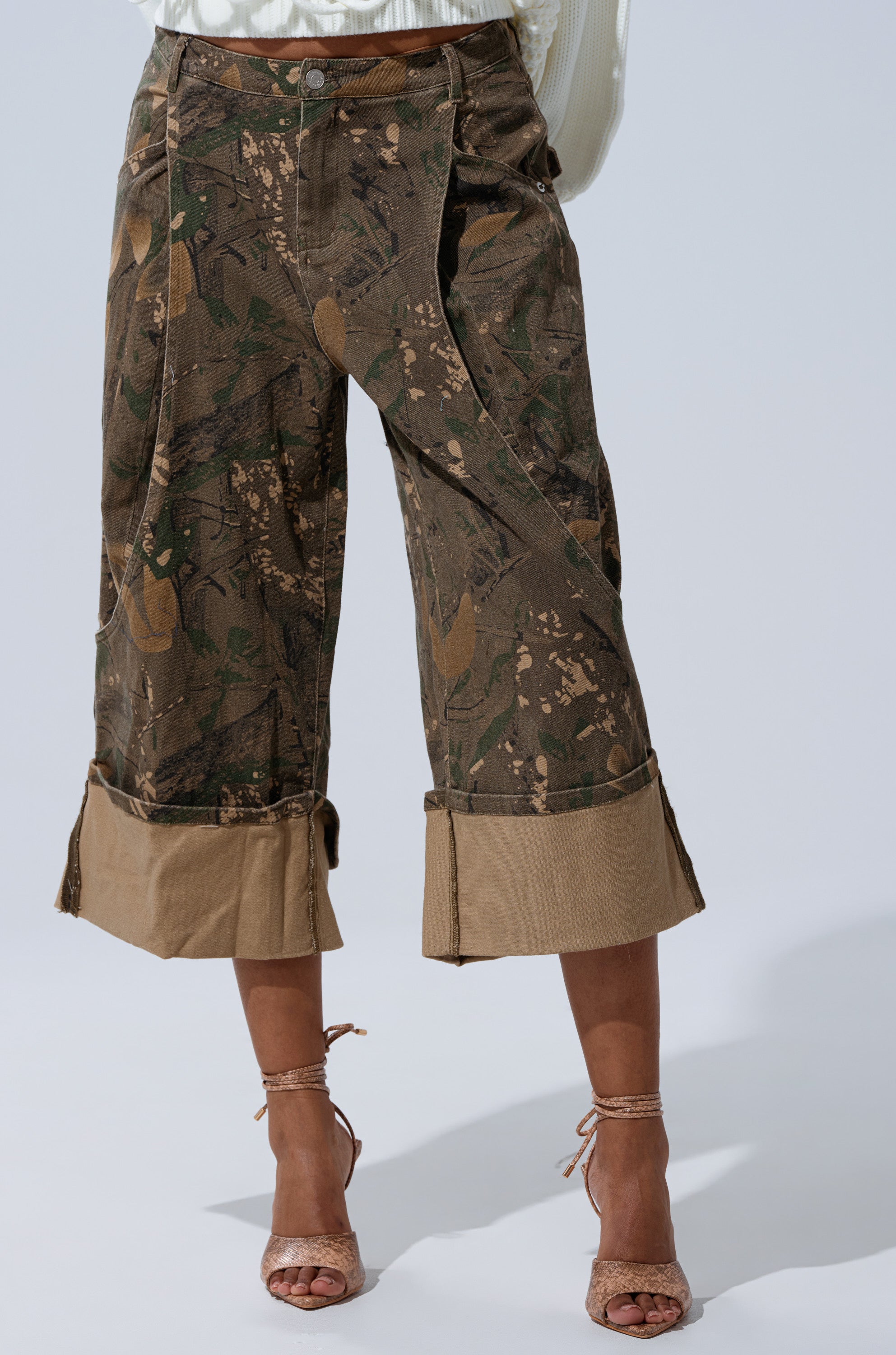 Someone wearing the Down and Dirty Camo Bermuda Short, featuring a mid-rise, wide-leg fit with beige cuffs, paired with beige high-heeled sandals and standing against a light background. 2