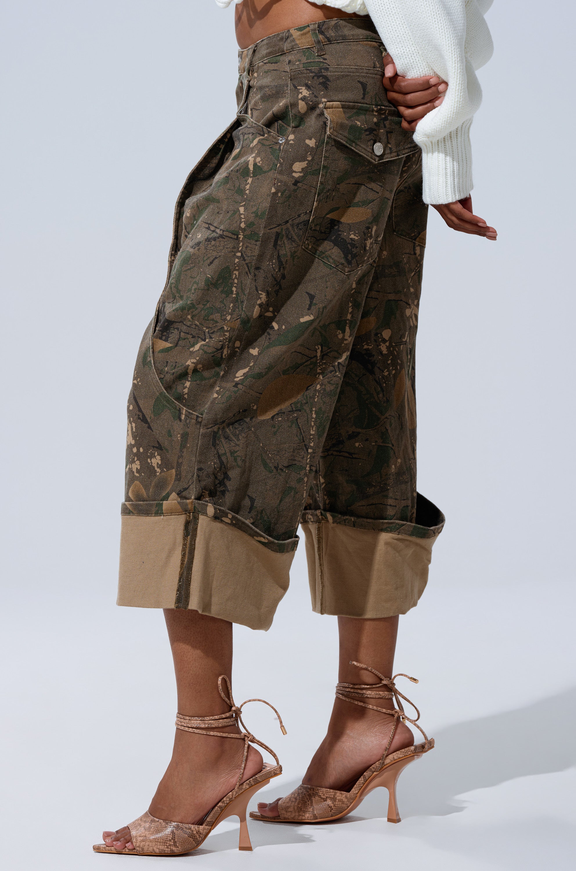 Model wears the DOWN AND DIRTY CAMO BERMUDA SHORT with a white knit sweater and strappy heeled sandals, mid-rise fit shown from the side against a plain background. 3