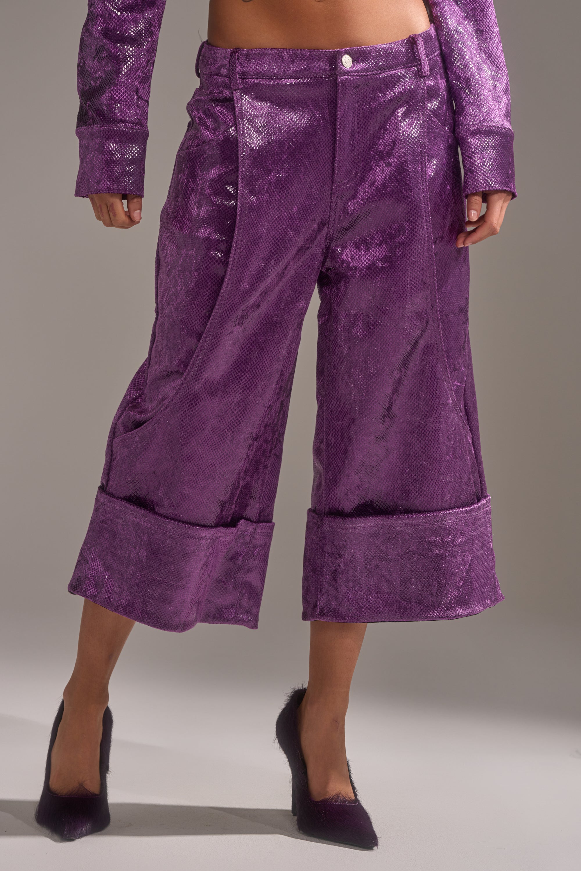 A person wearing the CRAZY TOUCH VELVET TROUSER in a shiny, rich purple with large cuffs and matching pointed-toe heels stands against a plain background.