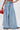 A person wearing THE BEST ONE YET WIDE LEG DENIM—vintage-inspired, high-rise wide-leg jeans with pleats—holds a small red handbag. Only the lower body is shown, paired with brown pointed shoes.