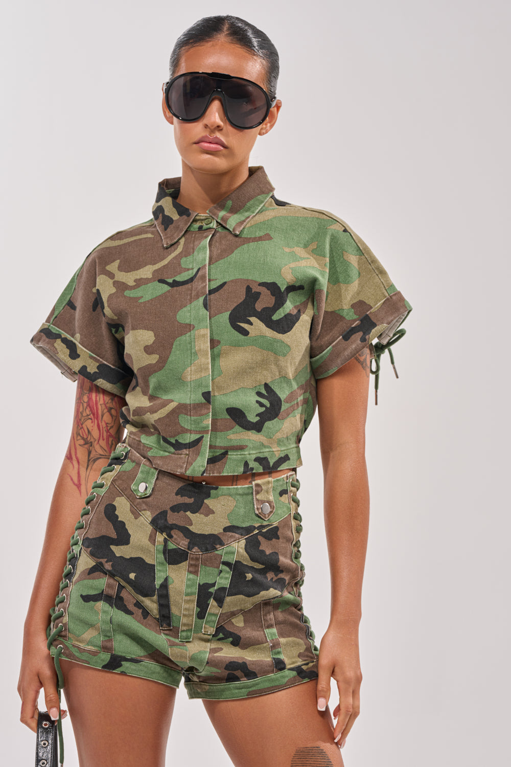 Wearing the I MEAN BUSINESS CAMO BUTTON DOWN, styled with large black sunglasses and high-waisted camouflage shorts, this look is effortlessly cool and perfect for street style against a plain background. 2