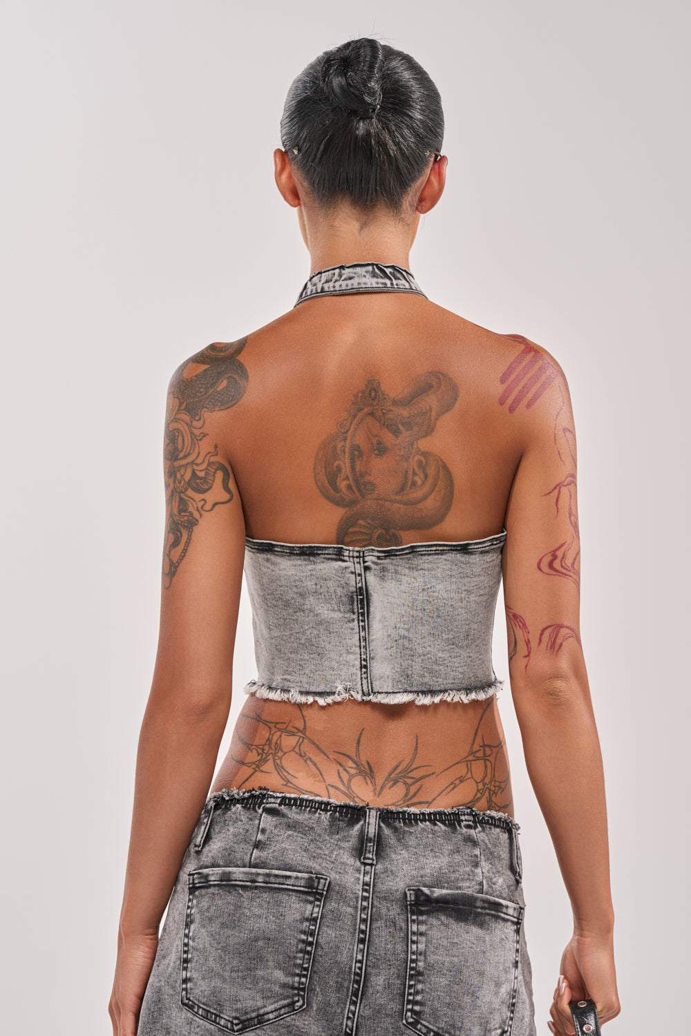 Person with short dark hair and tattoos on their back and arms wears the BREAK UP WITH HIM DENIM TOP, styled strapless with matching denim bottoms, facing away from the camera against a light background. 3
