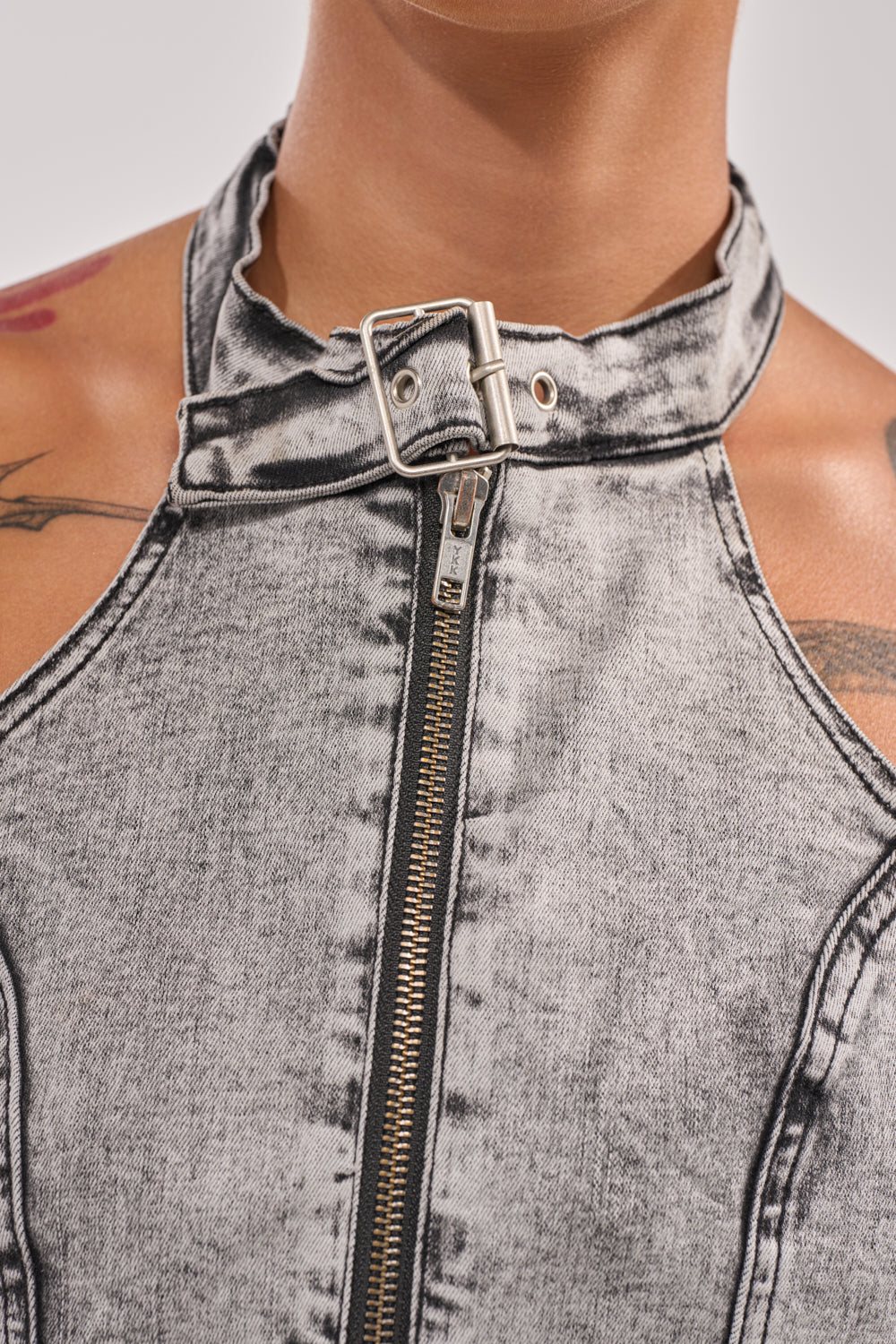Close-up of a person in the BREAK UP WITH HIM DENIM TOP—a sleeveless, washed grey halter with front zipper and buckled choker collar, showing shoulder tattoos for an edgy streetwear look. 6