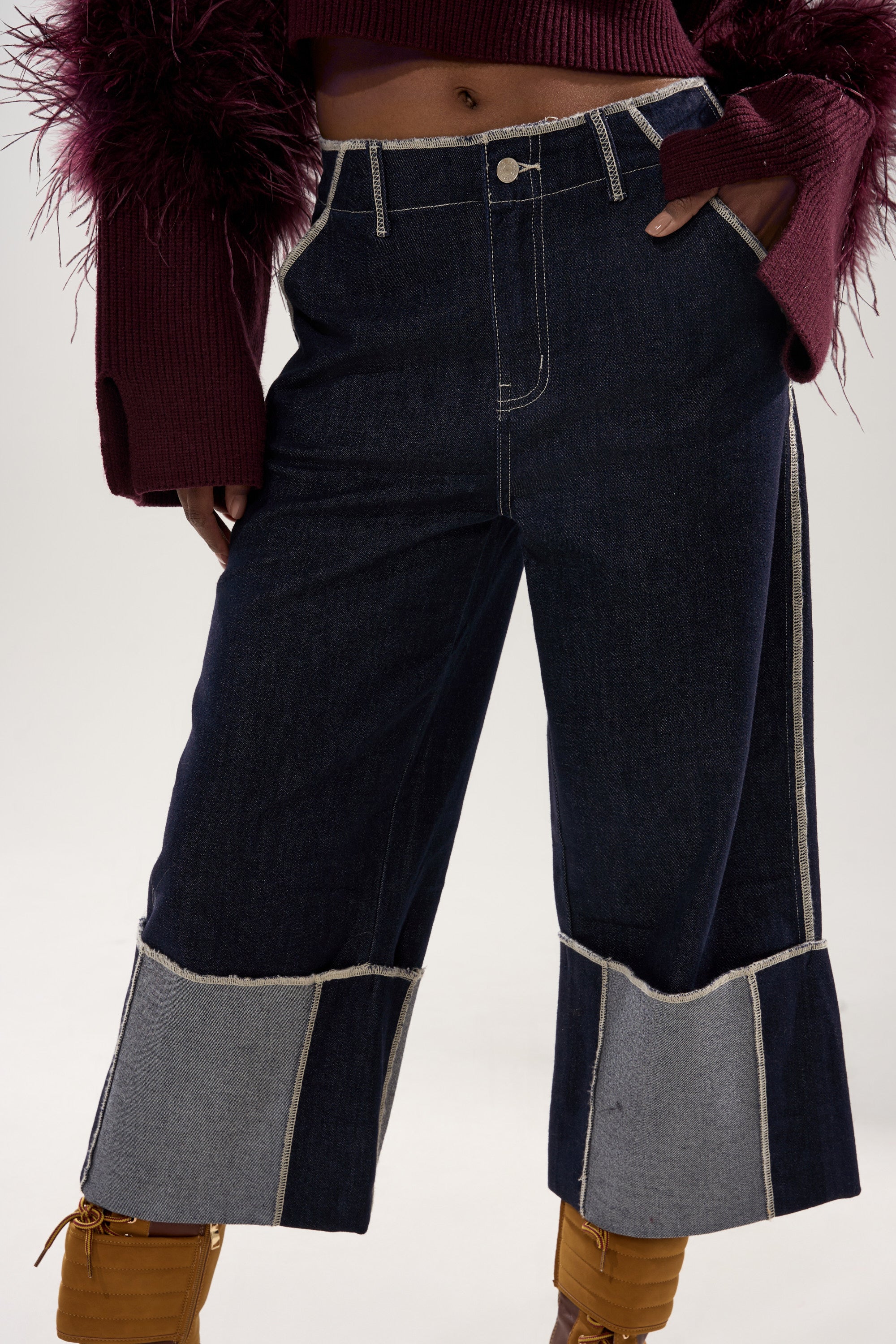 A person wearing the LOCKED UP DENIM BERMUDA SHORT paired with a burgundy sweater with feathered sleeves and tan lace-up boots. 5