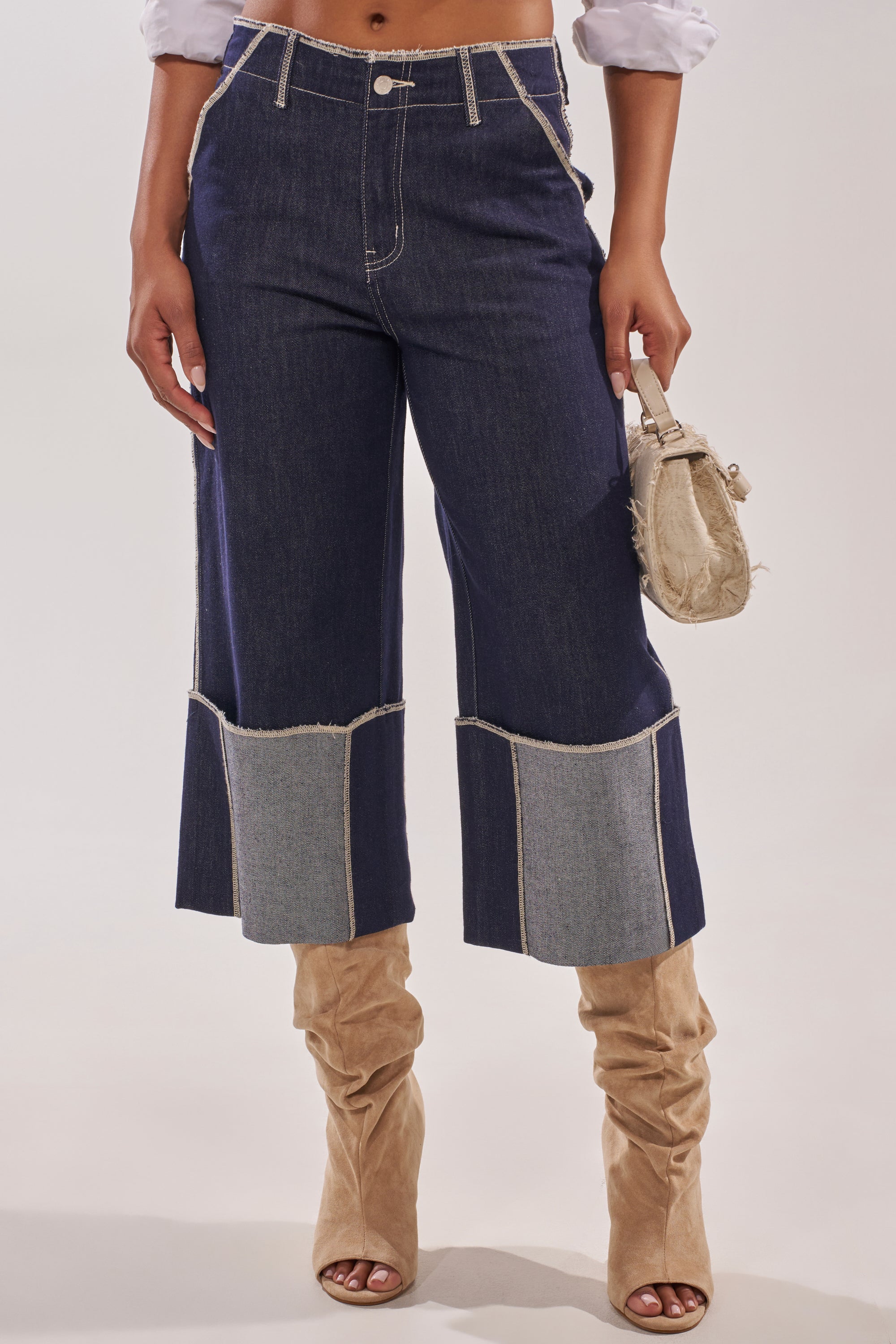 A woman wears the LOCKED UP DENIM BERMUDA SHORT, styled with slouchy tan suede knee-high boots, a small beige bag, and a rolled-sleeve shirt. 1