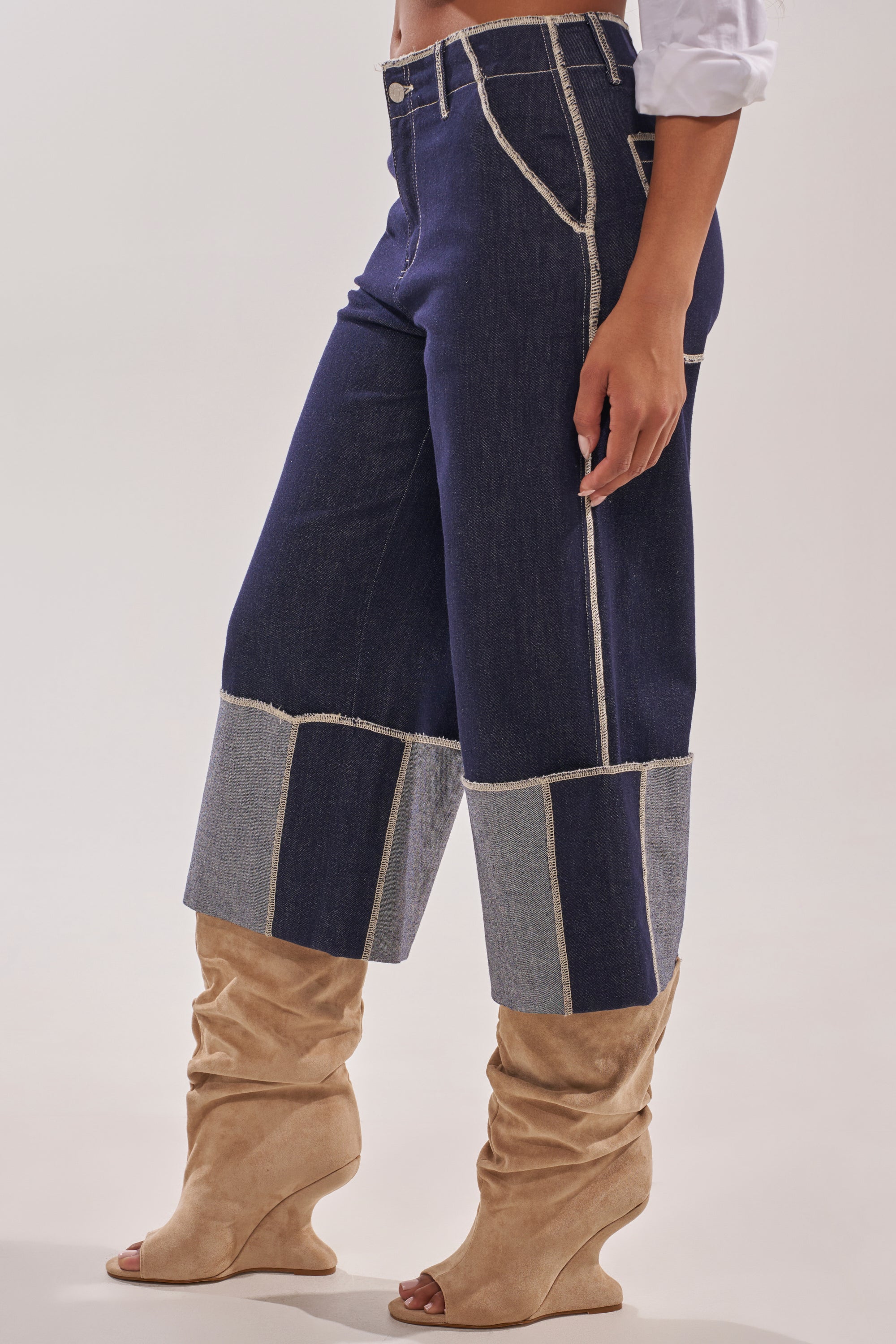 A person wears the LOCKED UP DENIM BERMUDA SHORT with visible seams and oversized cuffs, styled with beige slouchy wedge-heeled boots and a white shirt with rolled sleeves. 2