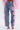 A person wearing FLOWER GIRLIE APPLIQUE DENIM JEANS with pink ruffled sheer side details, a pink textured top, and transparent pink high heels; the photo is taken from behind.