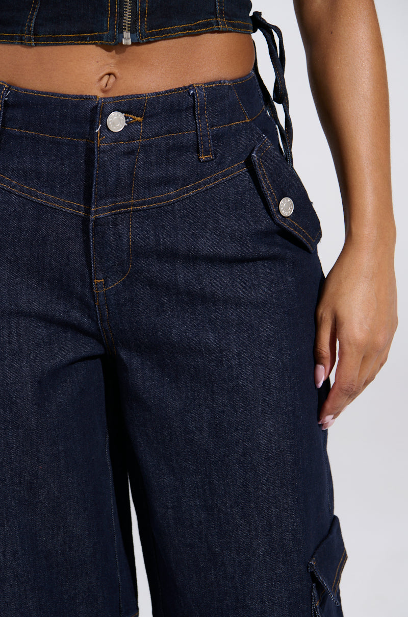 Close-up of a person wearing DENIM FOR DAYS DENIM PANT in dark blue with prominent stitching and metallic buttons, paired with a matching denim top. Their right hand rests at their side.