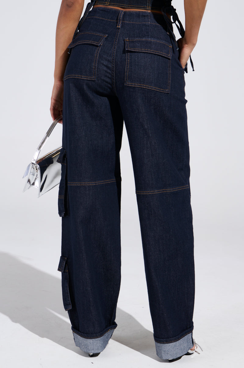 Person wearing the DENIM FOR DAYS DENIM PANT, featuring a high-rise fit, wide-leg silhouette, cuffed hems, and large cargo-style back pockets, holding a small metallic silver handbag. Photo taken from behind against a light background.