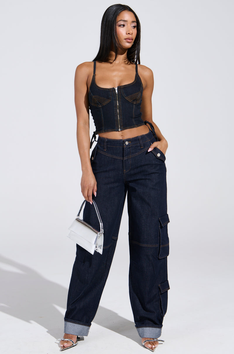A woman stands confidently in the DENIM FOR DAYS DENIM PANT with cargo-style pockets and rolled cuffs, paired with a black corset top, heels, a metallic handbag, and straight long hair against a plain light background.