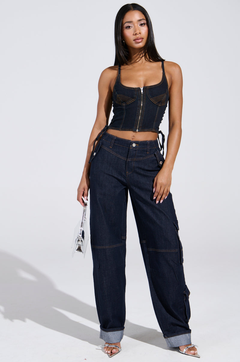 A woman poses in the DENIM FOR DAYS DENIM PANT—high-rise dark denim pants with cuffs—paired with a fitted black corset top, strappy heels, and a small clear handbag.