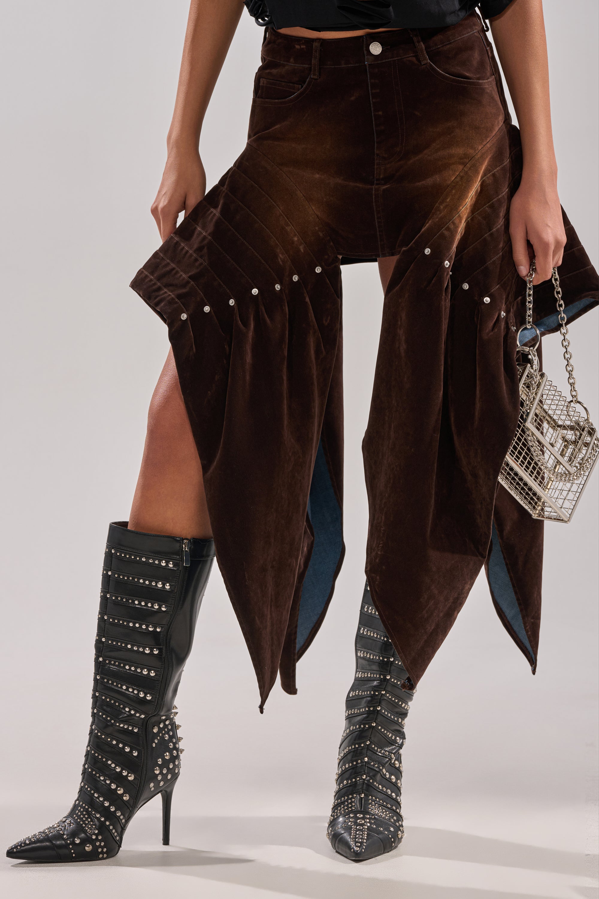 Wearing the ALL FOR IN VELVET DENIM MINI SKIRT, someone pairs it with black studded high-heeled boots and a small metallic handbag, posing against a light background.