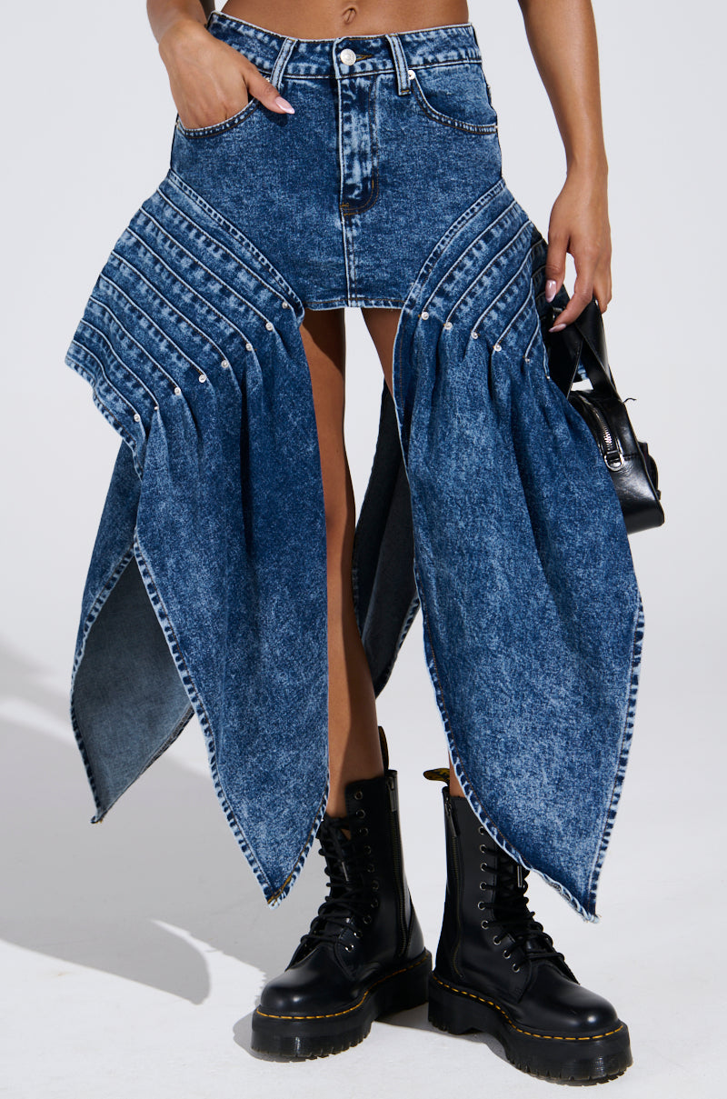 Someone is sporting the MOVE IN MOTION MINI SKIRT, with its unique paneled design resembling large leaves, in a medium blue wash. It's paired with black combat boots and a small black handbag.