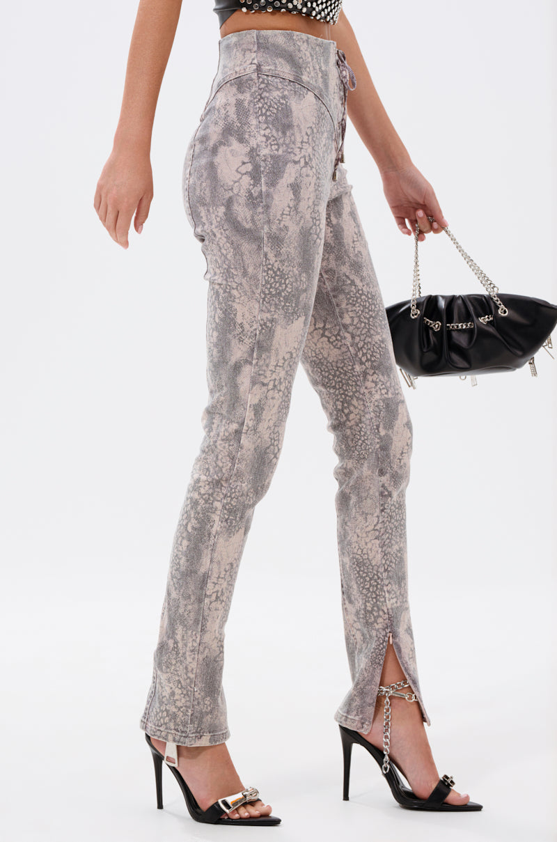 A person wears the IN THE SUN SNAKE LACE-UP PANT—high-rise, gray snake-print with front ankle slits—paired with black high-heeled sandals featuring gold buckles and a black chain-detailed handbag, set against a plain white background. 4