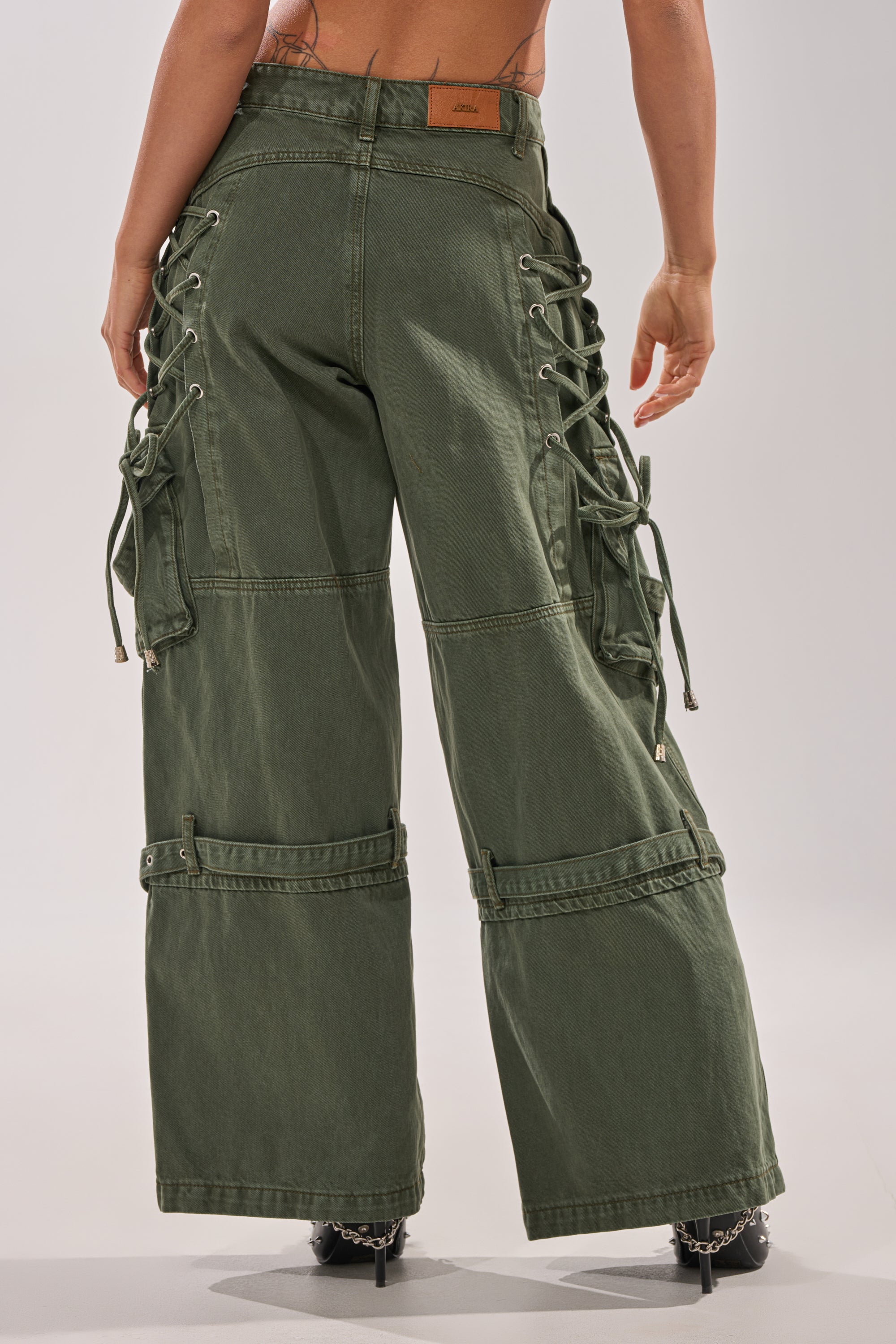 A person shown from the back wearing the KARA CARGO DENIM—olive, high-waisted, wide-leg pants with lace-up sides, large pockets, adjustable straps, and a loose fit for comfort and style. 5