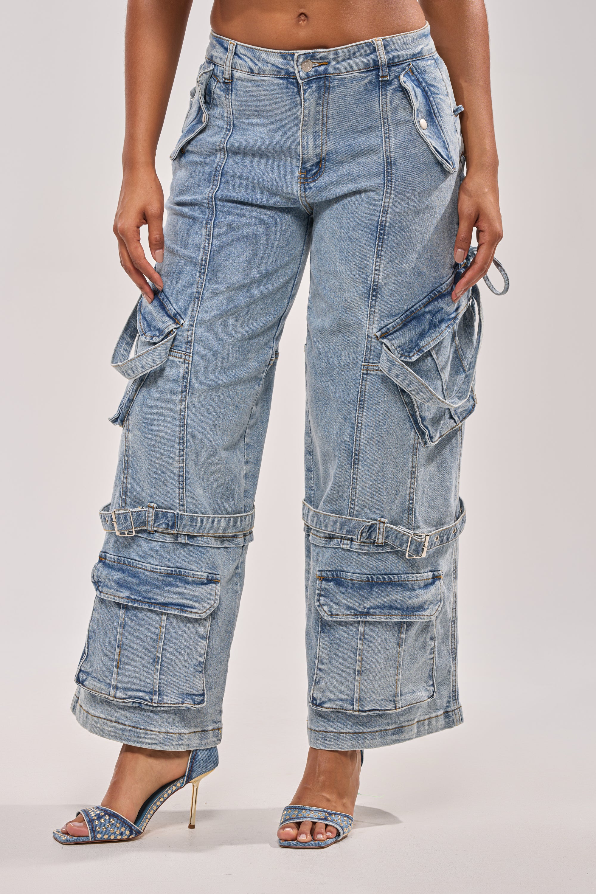 A person wearing the KARA DENIM CARGO PANT with multiple pockets, adjustable buckles, and straps, styled with open-toe heels featuring rhinestone accents. 6