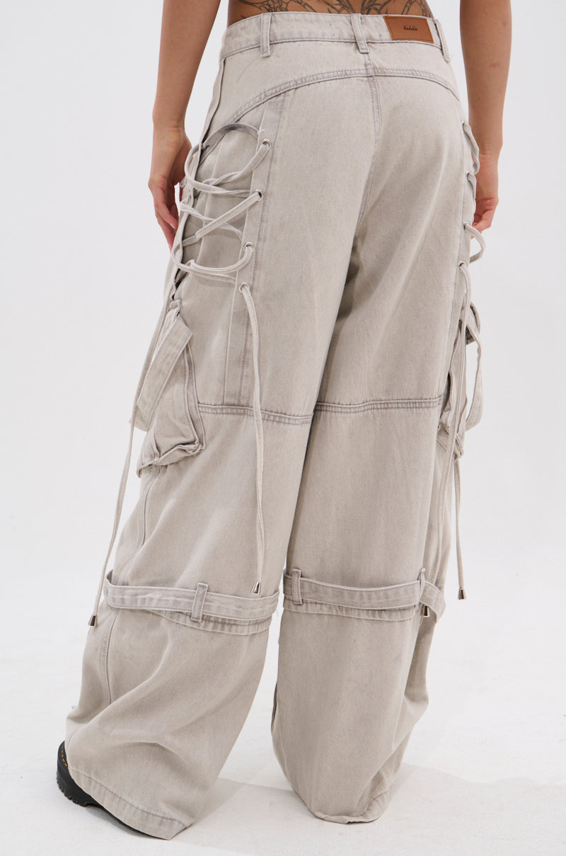 A person is seen from the back wearing the KARA DENIM CARGO PANT in light beige, featuring a high-rise fit, ultra-wide leg, large cargo pockets, and side lace-up details, set against a plain white background.