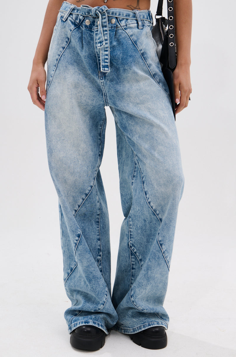 Wearing the TIED TO YOU RELAXED DENIM PANT WITH TIE BELT, black shoes, and a black shoulder bag, a person stands against a plain white background.