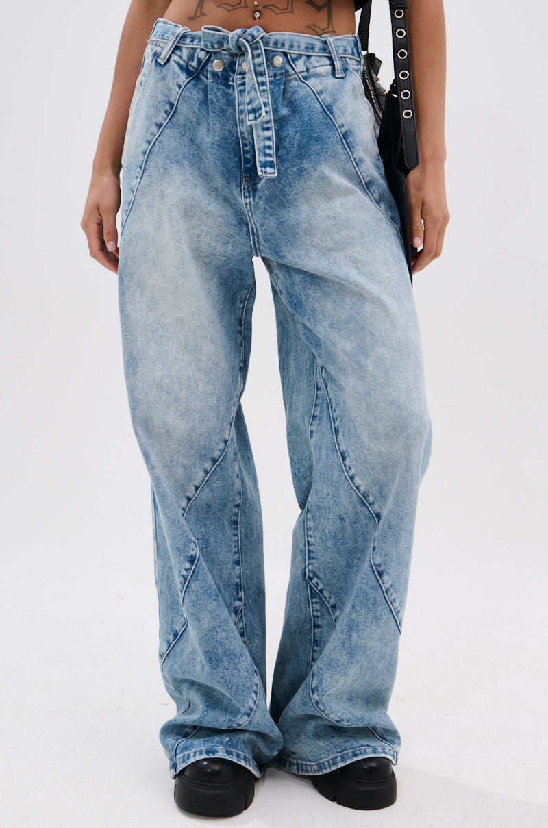 Model wears the TIED TO YOU RELAXED DENIM PANT WITH TIE BELT, a light wash, high-rise, wide-leg jean featuring a tie-belt waist. The focus is on the pant’s relaxed fit and faded denim texture. Upper body is partially visible; paired with black chunky shoes.