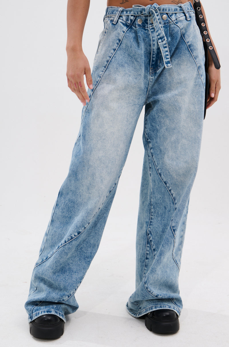 Wearing the TIED TO YOU RELAXED DENIM PANT WITH TIE BELT in a light wash, styled high-rise and wide-leg, paired with black shoes. Only the lower half of the body is visible against a plain white background.